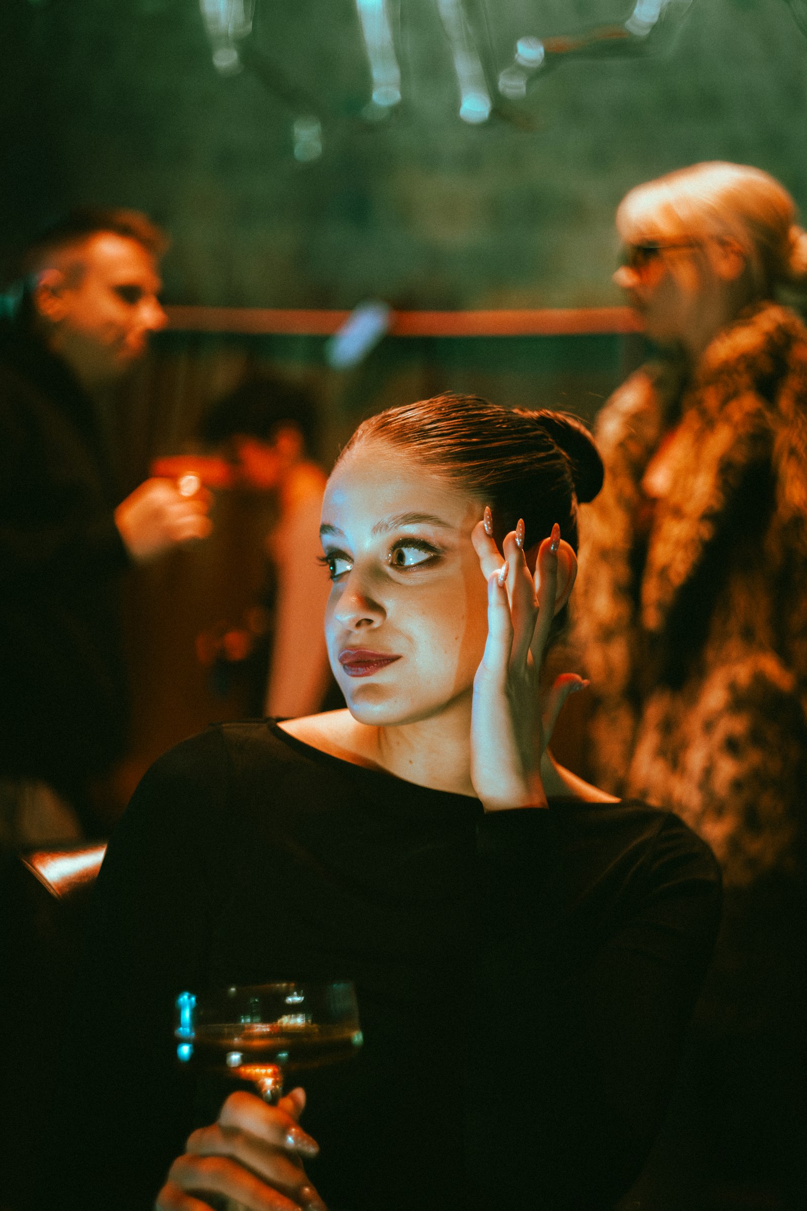 Woman with her hair in a sleek low bun holding a drink in a warm, dimly lit bar