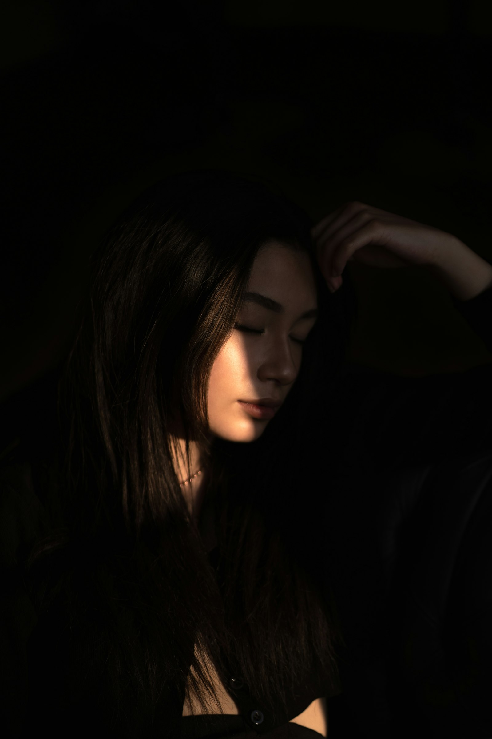 Yuki Tanaka with long straight dark hair, lit by a single narrow light against a near-black frame